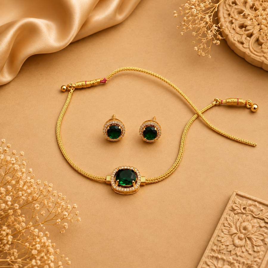 A gold-plated necklace and matching earring set featuring vibrant green emerald stones encircled by sparkling white crystals, displayed on a beige surface with satin and floral accents. Available in the UK at theindianshelf.co.uk.