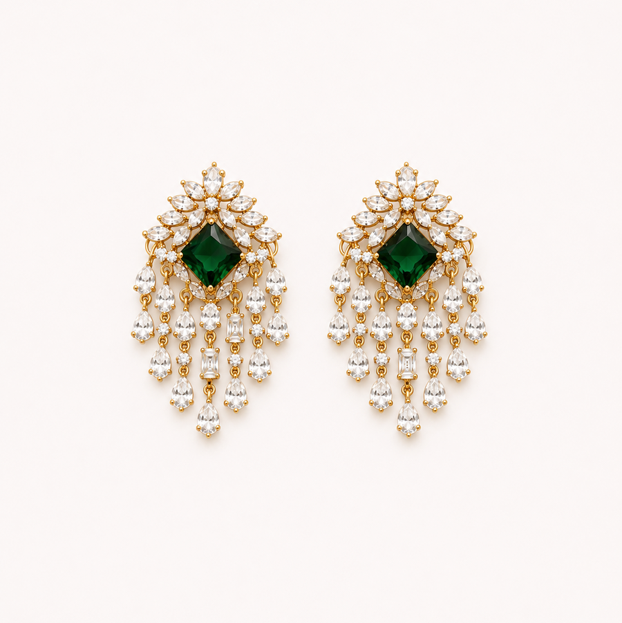 A pair of premium gold-plated chandelier drop earrings featuring a central square emerald green stone bordered by clear American Diamond crystals and cascading teardrop dangles, centered on a solid white background. Available in the UK at theindianshelf.co.uk.