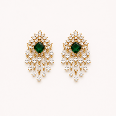 A pair of premium gold-plated chandelier drop earrings featuring a central square emerald green stone bordered by clear American Diamond crystals and cascading teardrop dangles, centered on a solid white background. Available in the UK at theindianshelf.co.uk.