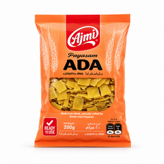 A professional studio product shot of a 200g vertical pillow pouch of Ajmi Payasam Ada standing upright against a solid white background The packaging is designed with a bright orange theme, featuring a bold red vertical band at the top center containing the white "Ajmi" logo. The product name "Payasam ADA" is printed boldly across the upper half in black. This product is available in the UK at theindianshelf.co.uk.