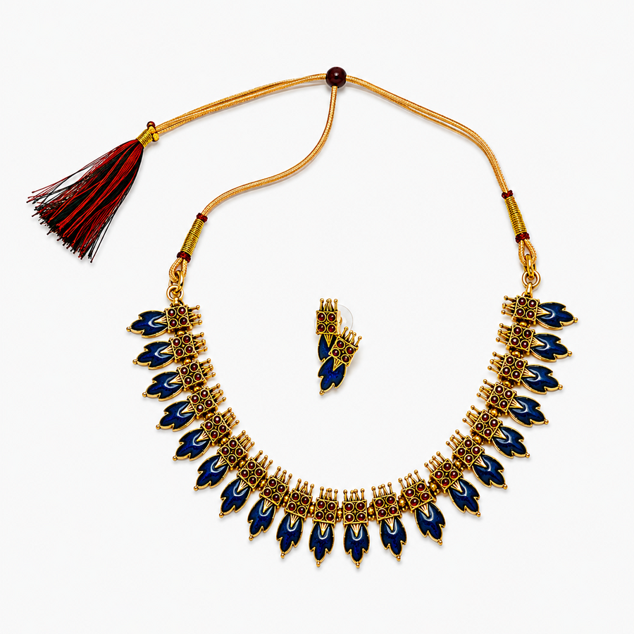 An antique gold-plated traditional jewelry set including a leaf-motif choker necklace and matching earrings adorned with dark blue enamel inlays and mini red stones, centered on a solid white background. Available in the UK at theindianshelf.co.uk.