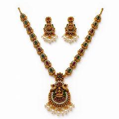 A studio product shot of an antique gold-plated Temple Jewelry Set isolated on a white background. The long necklace and matching earrings feature a Goddess Laxmi pendant decorated with red, green, and white stones and finished with dangling pearls. Available in the UK at theindianshelf.co.uk.