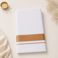 A studio flatlay shot of a neatly folded white Kerala Double Mundu on a light cream surface. The cotton fabric features a horizontal border with a thick copper zari band and a matching thin pinstripe. Dried floral sprigs and a small gold dish sit in the corners. Available in the UK at theindianshelf.co.uk.