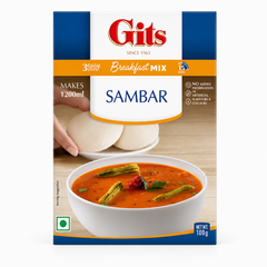 A 100g box of Gits Sambar Breakfast Mix centered on a solid white background, featuring a blue and orange border with the red Gits logo, product details highlighting "3 Easy Steps in 15 mins," and a serving suggestion showing a white bowl of sambar garnished with drumsticks alongside soft white idlis in the background. This product is available in the UK at theindianshelf.co.uk.