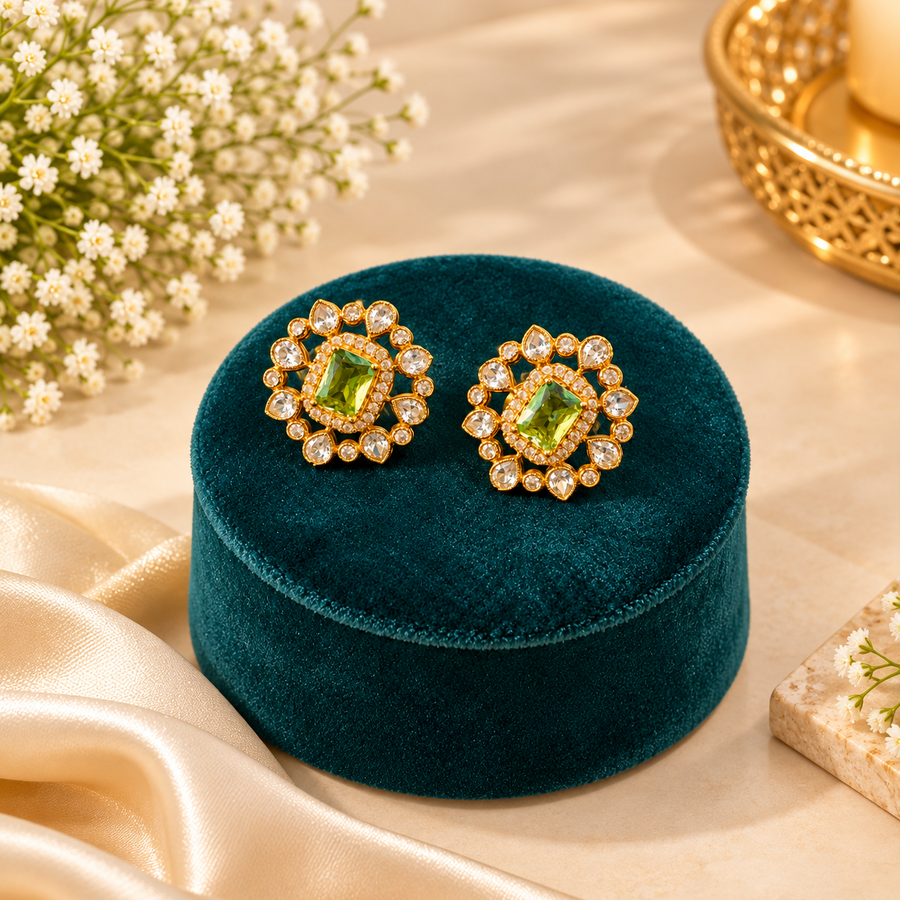 Gold-plated floral stud earrings centered with a peridot-green stone and surrounded by uncut white stones on a teal velvet box. Available in the UK at theindianshelf.co.uk.