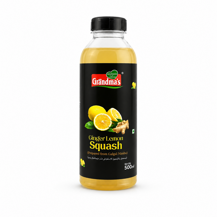 A professional studio product shot of a 500ml bottle of Grandma's Ginger Lemon Squash isolated against a pure white background in image_924956.png. The transparent bottle reveals a light golden-yellow liquid inside and features a bold black label decorated with graphics of whole and halved fresh lemons, a piece of ginger root, and the red and green brand logo.