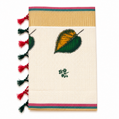 A vertically folded off-white tissue saree centered on a solid white background, featuring fine grid check patterns, a hand-painted yellow and green leaf motif, a small green floral sprig, a wide golden kasavu border with pink and teal accent stripes, and alternating pink and dark green knotted fringe tassels along the left edge. Available in the UK at theindianshelf.co.uk.