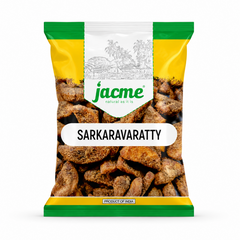 A professional studio product shot of a clear pillow pouch filled with rustic, jaggery-coated Jacme Sarkaravaratty chunks isolated against a pure white background. The clean packaging features a white, yellow, and green header label showing a traditional village sketch above the prominent product name.