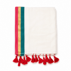 A neatly folded off-white mulcotton saree centered on a solid white background, featuring a tri-color vertical border with magenta pink, golden kasavu, and teal green stripes, finished with bright red handcrafted tassels along the bottom fringe. Available in the UK at theindianshelf.co.uk.