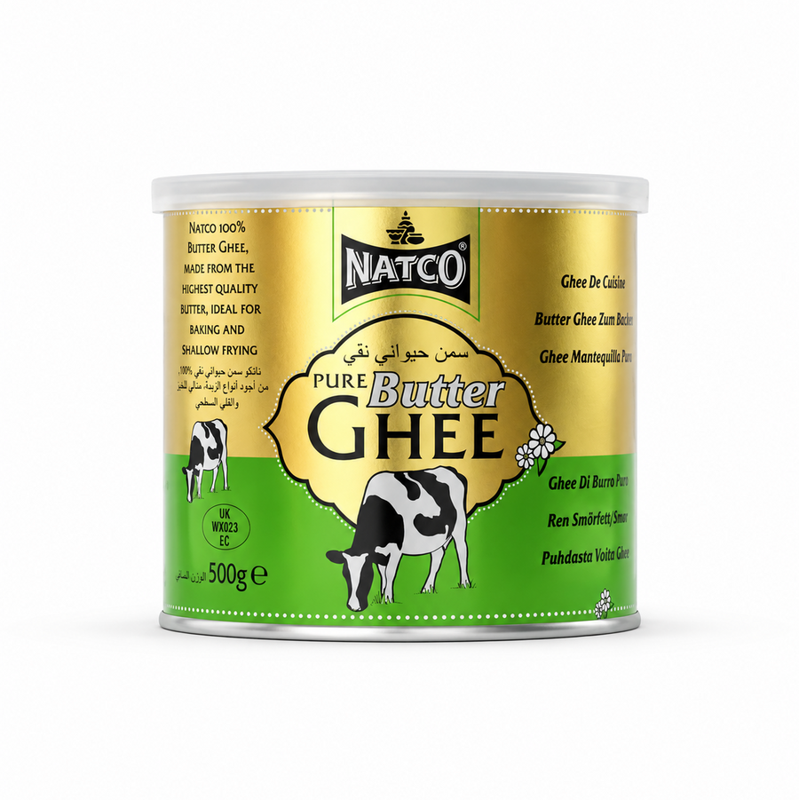 A studio product shot of a cylindrical 500g tin of Natco Pure Butter Ghee standing vertically against a solid white background The tin features a half-metallic-gold and half-bright-green split color scheme, capped by a semi-translucent plastic lid. The top center displays the black "NATCO" corporate shield logo. Below it, inside a golden ornate frame, the text reads "PURE Butter GHEE" alongside its Arabic translation. This product is available in the UK at theindianshelf.co.uk.