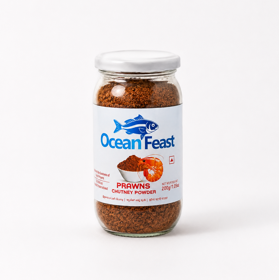 A studio product shot of a 200g glass jar of Ocean Feast Prawns Chutney Powder against a white backdrop. The glass container displays a coarse brown spice mix below a white label featuring a blue fish logo and an illustration of a prawn. Available in the UK at theindianshelf.co.uk.
