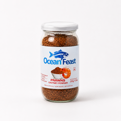 A studio product shot of a 200g glass jar of Ocean Feast Prawns Chutney Powder against a white backdrop. The glass container displays a coarse brown spice mix below a white label featuring a blue fish logo and an illustration of a prawn. Available in the UK at theindianshelf.co.uk.