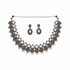 A studio product shot of an antique oxidized silver Choker Necklace and Earrings Set isolated on a white background. The jewelry features sculpted floral metalwork details set with clear white stones. Available in the UK at theindianshelf.co.uk.