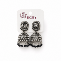 A studio product shot of a pair of antique silver oxidized Rossy Jhumka Earrings on a white display card. The dome earrings feature rows of white crystals and a fringe of small black beads. Available in the UK at theindianshelf.co.uk.