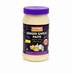 A 1kg clear plastic jar of Sapna Ginger Garlic Paste centered on a solid white background, featuring a vibrant purple ribbed screw cap and a black label showcasing graphics of fresh ginger root, garlic bulbs, and the red Sapna brand logo.