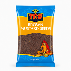 A 100g pouch of TRS Brown Mustard Seeds centered on a solid white background, featuring a vibrant yellow and blue packaging design with the TRS logo and a clear window showing small brown mustard seeds next to an illustration of a traditional Indian woman. This product is available in the UK at theindianshelf.co.uk.