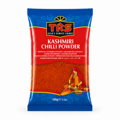 A 100g pouch of TRS Kashmiri Chilli Powder centered on a solid white background, featuring a vibrant red and blue packaging design with the TRS logo and a clear window showing rich, finely ground red chilli powder next to an illustration of a traditional Indian woman. This product is available in the UK at theindianshelf.co.uk.
