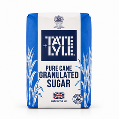 A paper bag of Tate & Lyle Pure Cane Granulated Sugar centered on a solid white background, featuring a blue and white packaging design with sugar cane illustrations, the Union Jack flag, and a recyclable packaging seal. This product is available in the UK at theindianshelf.co.uk.