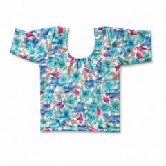 A turquoise and blue floral print readymade stretchable saree blouse displayed flat on a solid white background, featuring short sleeves, a scoop neck, and magenta leaf accents throughout the pattern. Available in the UK at theindianshelf.co.uk.