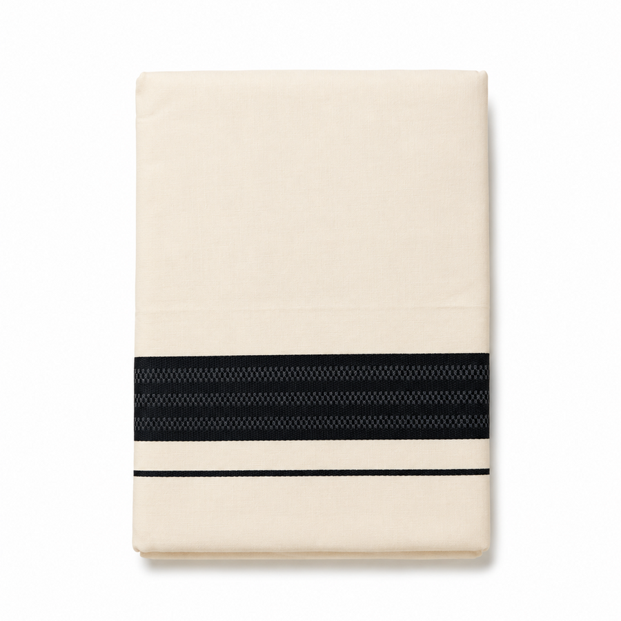A neatly folded cream men's Kerala mundu (dhoti) centered on a solid white background, featuring a wide horizontal textured black woven border (kara) and a thin parallel black accent stripe near the bottom edge. Available in the UK at theindianshelf.co.uk.