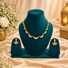A gold-plated crescent moon American diamond necklace and matching earring set displayed on a deep teal velvet bust against a warm, decorative background. Available in the UK at theindianshelf.co.uk.