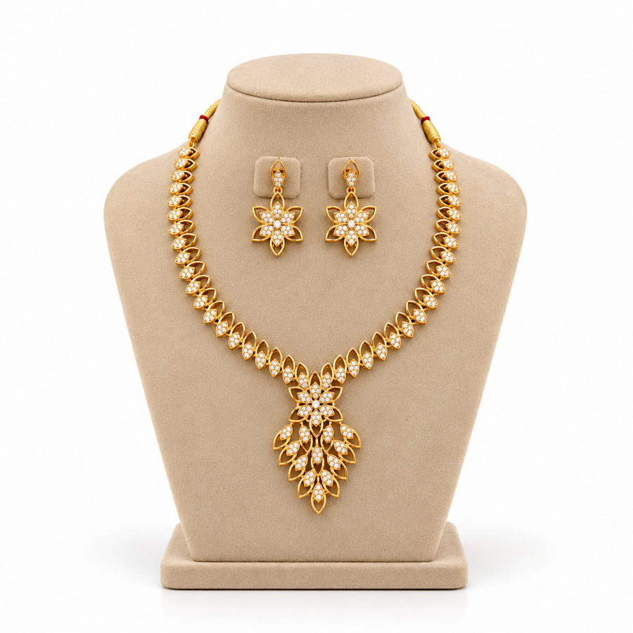 A gold-plated necklace set featuring an elaborate floral leaf cluster pendant encrusted with white CZ stones, displayed on a beige velvet mannequin bust. Available in the UK at theindianshelf.co.uk.