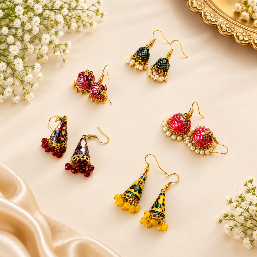 An assortment of handcrafted colorful Meenakari enamel jhumka earrings with beaded fringes displayed on a cream background with flowers. Available in the UK at theindianshelf.co.uk.
