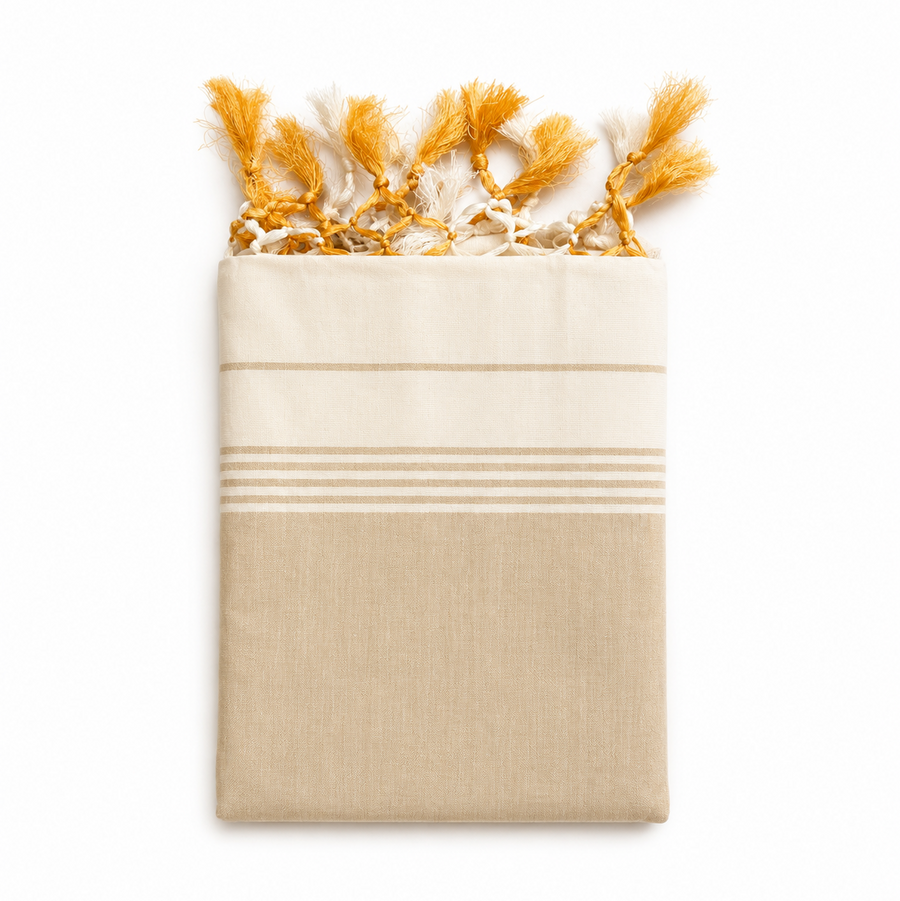 A neatly folded traditional off-white Kerala tissue saree centered on a solid white background, featuring a subtle beige lower section, fine horizontal stripes, and handcrafted yellow and white knotted tassels along the top edge.