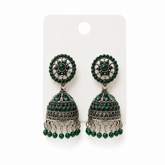 A studio product shot of a pair of antique silver oxidized Jhumka Earrings pinned to a white card against a white background from image_256199.jpg. The drop earrings feature a detailed dome bell accented with green stones and beads. Available in the UK at theindianshelf.co.uk.