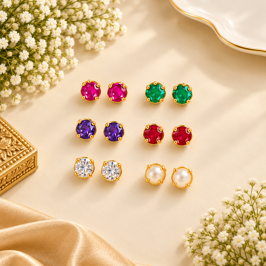 A collection of six pairs of colourful gemstone and pearl stud earrings set in polished gold prongs, arranged neatly on a warm neutral background. Available in the UK at theindianshelf.co.uk.