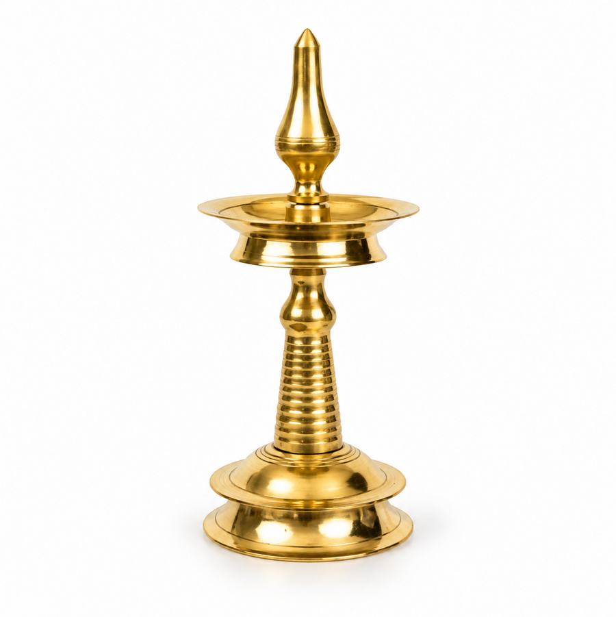 A 10-inch traditional brass Kerala kuthu vilakku standing oil lamp with a round base and polished golden finish, centered on a solid white background. Available in the UK at theindianshelf.co.uk.