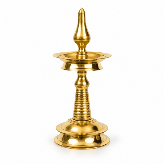 A 10-inch traditional brass Kerala kuthu vilakku standing oil lamp with a round base and polished golden finish, centered on a solid white background. Available in the UK at theindianshelf.co.uk.
