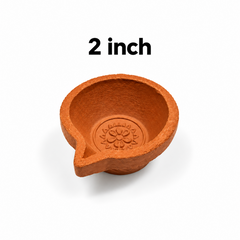 A 2-inch single-face terracotta mud lamp (agal vilakku) featuring a small embossed flower motif at the base, centered on a solid white background with a "2 inch" label above it. Available in the UK at theindianshelf.co.uk.