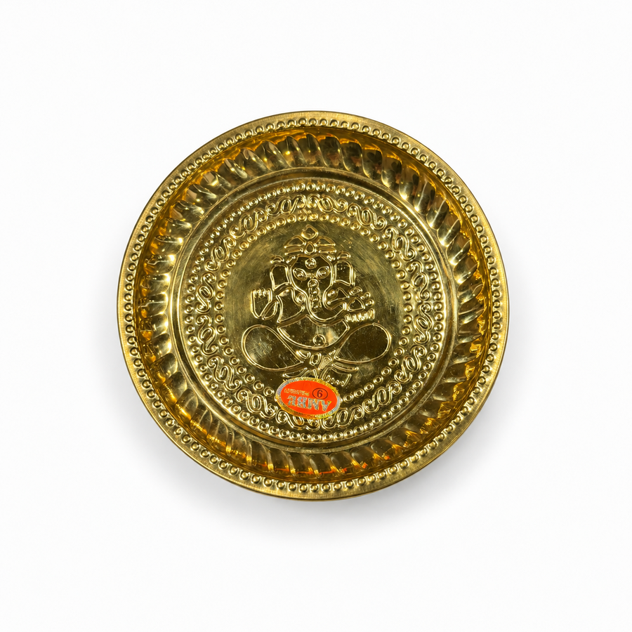 A 9-inch brass puja plate featuring an embossed motif of Lord Ganesha at the center and a decorated rim, centered on a solid white background. Available in the UK at theindianshelf.co.uk.