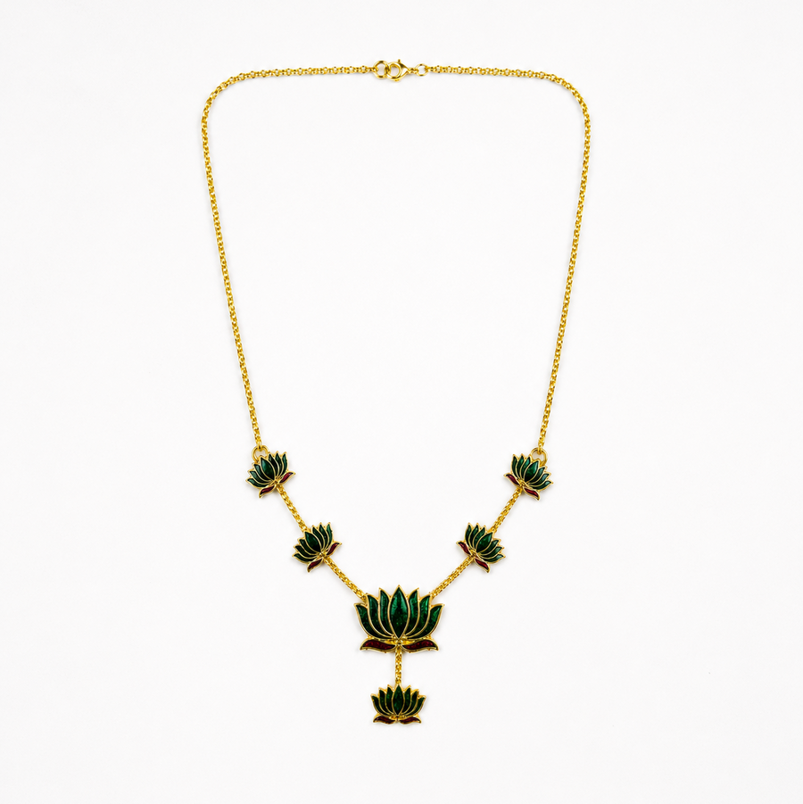 A delicate gold-plated chain necklace featuring multiple emerald-green enamel lotus motifs arranged along the bottom, centered on a solid white background. Available in the UK at theindianshelf.co.uk.