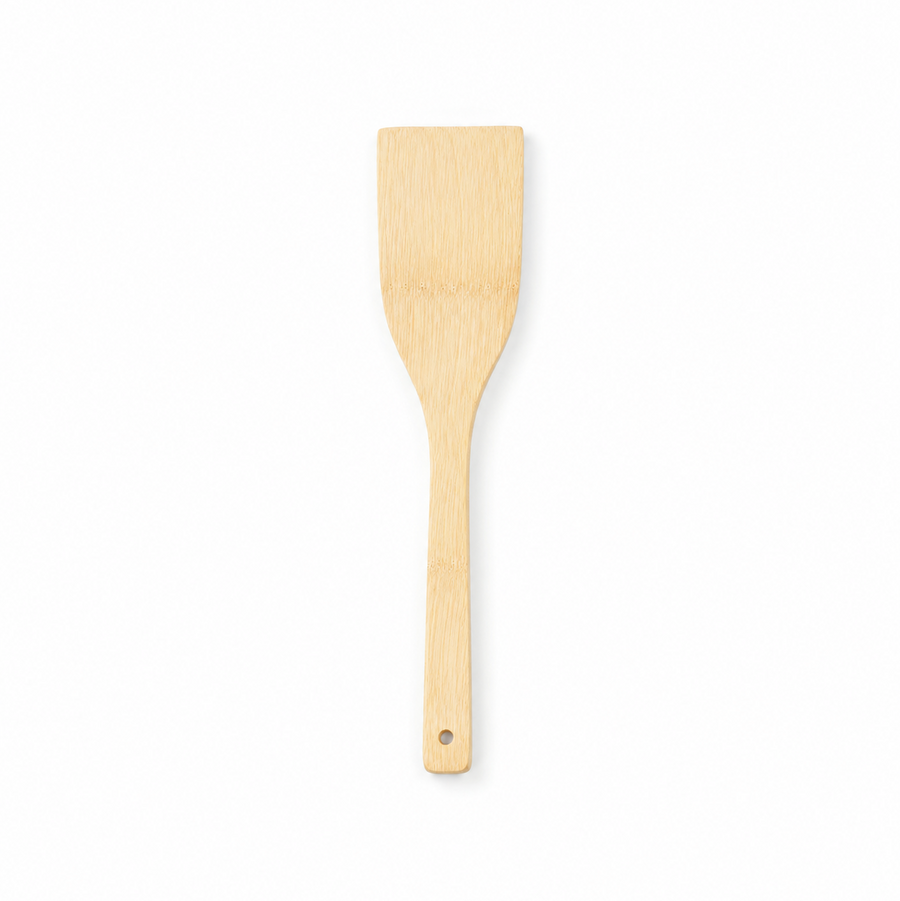 A natural light wood flat cooking spatula turner with a hanging hole at the handle tip, displayed vertically against a solid white background. Available in the UK at indianshelf.co.uk.