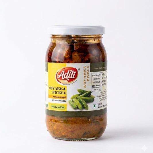 Aditi Kovakka Pickle
A vertical studio shot of a clear glass jar filled with Aditi Kovakka (Ivy Gourd) Pickle. The jar features a white screw-top lid and a yellow-and-white label with a red "Aditi" logo. A small image on the label shows a pile of fresh, green whole ivy gourds. The pickle inside consists of sliced green ivy gourd pieces submerged in a thick, textured, orange-brown spice paste. The jar is set against a clean, plain white background.This product is available in the UK at theindianshelf.co.uk.