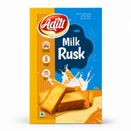 A studio product shot of a rectangular cardboard box of Aditi Milk Rusk against a solid white background. The packaging features a vertical split design, with a striped golden-orange pattern on the left and a solid bright blue background on the right. The upper left displays the red and yellow oval "Aditi" logo. The center bears the prominent white title "Milk Rusk" set against a dark blue fluid background accent. This product is available in the UK at theindianshelf.co.uk.