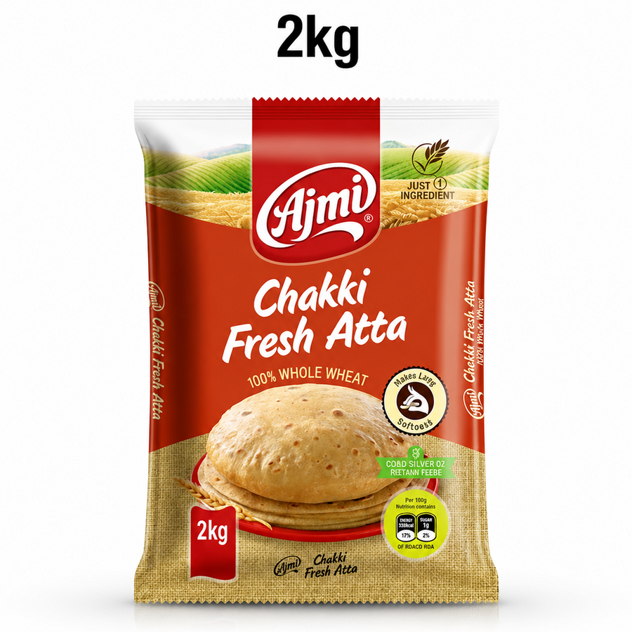 A professional studio product shot of a 2kg pillow pouch of Ajmi Chakki Fresh Atta standing vertically against a solid white background, with a "2kg" text label floating centered above it. The upper portion of the package shows a lush illustration of golden wheat fields beneath a clear sky, segmented by a central red stripe housing the white "Ajmi" logo. This product is available in the UK at theindianshelf.co.uk.