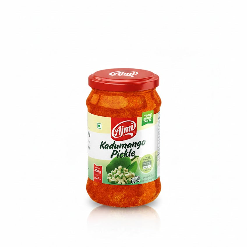 This image displays a glass jar of Ajmi Kadumango Pickle (Raw Mango Pickle), which has a red lid and a label indicating a Net Wt. 400g. The label features the Ajmi brand name and a picture of small, diced green mango pieces. The pickle itself is a rich, reddish-orange color, visible through the jar. This traditional Indian condiment is sold internationally and is available through various retailers, including those like The Indian Shelf UK.