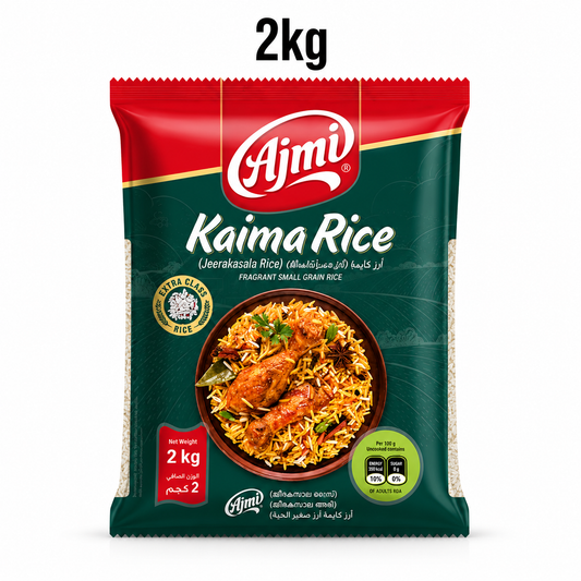A professional studio product shot of a 2kg pillow pouch of Ajmi Kaima Rice standing vertically against a solid white background, underneath a bold "2kg" The top section of the bag features a red curved panel that houses the white "Ajmi" logo. The main body of the packaging is a deep forest green color, accented with a faint line illustration of rolling hills and agricultural fields. This product is available in the UK at theindianshelf.co.uk.