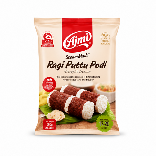 A professional studio product shot of a vertical 500g pillow pouch of Ajmi Steam Made Ragi Puttu Podi against a solid white background. The packaging features a light cream background with a prominent red vertical block at the top center housing the white "Ajmi" logo. Below the logo, the product name "Steam Made Ragi Puttu Podi" is printed in elegant dark brown script. This product is available in the UK at theindianshelf.co.uk.