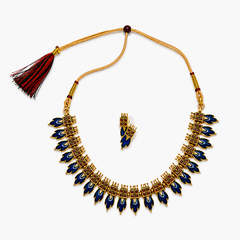 An antique gold-plated traditional jewelry set including a leaf-motif choker necklace and matching earrings adorned with dark blue enamel inlays and mini red stones, centered on a solid white background. Available in the UK at theindianshelf.co.uk.