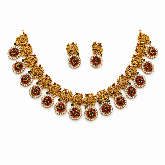 A studio product shot of an antique gold-plated Temple Jewelry Choker Set isolated on a white background from image_257100.jpg. The choker and matching drop earrings feature intricate peacock motifs and circular pendants accented with red, green, and white stones. Available in the UK at theindianshelf.co.uk.