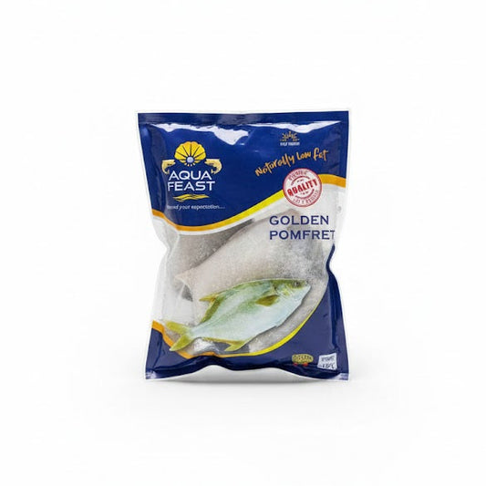 A blue and white vacuum-sealed bag of Aqua Feast Golden Pomfret. The packaging highlights that the fish is "Naturally Low Fat" and "Premium Quality." A clear window in the center displays the frozen whole fish, while a colorful illustration of a golden pomfret is featured at the bottom.This seafood product is available for purchase in the UK at theindianshelf.co.uk.