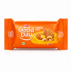 A professional studio product shot of a horizontally oriented bright orange flow-wrap plastic pack of Britannia Good Day Cashew Cookies against a clean white background. The front showcases the prominent white "Good Day" brand logo underscored by a sweeping white-and-red smile graphic. To the right, a realistic illustration features two golden-brown, ridge-patterned cookies alongside a curl of fresh butter and whole roasted cashew nuts. This product is available in the UK at theindianshelf.co.uk.