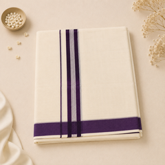 A studio flatlay of a neatly folded cream Kerala Double Mundu on a light textured background. The cotton textile features a distinct horizontal border with deep purple bands and fine lavender pinstripes. A small dish of white beads and dried flowers decorate the corners. Available in the UK at theindianshelf.co.uk.