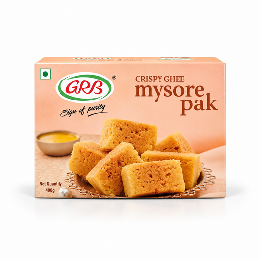 A 400g retail box of GRB Crispy Ghee Mysore Pak featuring brand logos and an arrangement of golden sweet pieces, centered on a solid white background. Available in the UK at theindianshelf.co.uk.