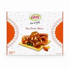 A professional studio product shot of a square white cardboard outer box for GRB Dry Fruits Halwa against a solid white background. The packaging features a delicate pattern of small brown dots, framed on the left and right edges by large, decorative orange mandala semi-circles. At the top center sits the oval green-and-red "GRB" logo above the script text "Sign of purity" and the brown product title "Dry Fruits Halwa".This product is available in the UK at theindianshelf.co.uk.