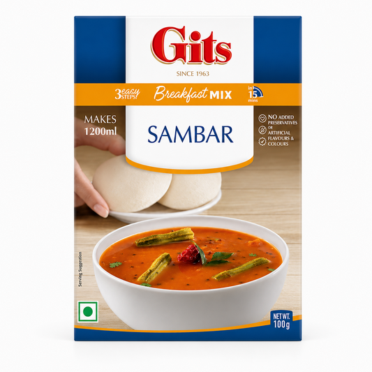 A 100g box of Gits Sambar Breakfast Mix centered on a solid white background, featuring a blue and orange border with the red Gits logo, product details highlighting "3 Easy Steps in 15 mins," and a serving suggestion showing a white bowl of sambar garnished with drumsticks alongside soft white idlis in the background. This product is available in the UK at theindianshelf.co.uk.